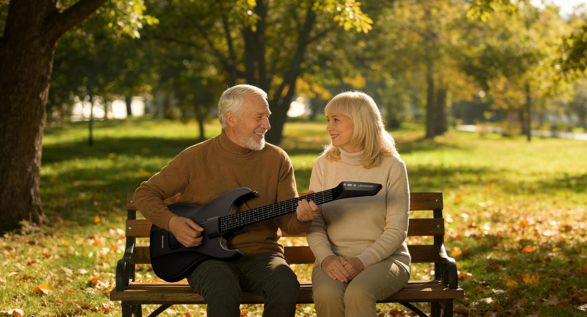 An elderly man plays an Aeroband Guitar on a park bench while smiling at a woman during a sunny autumn day
