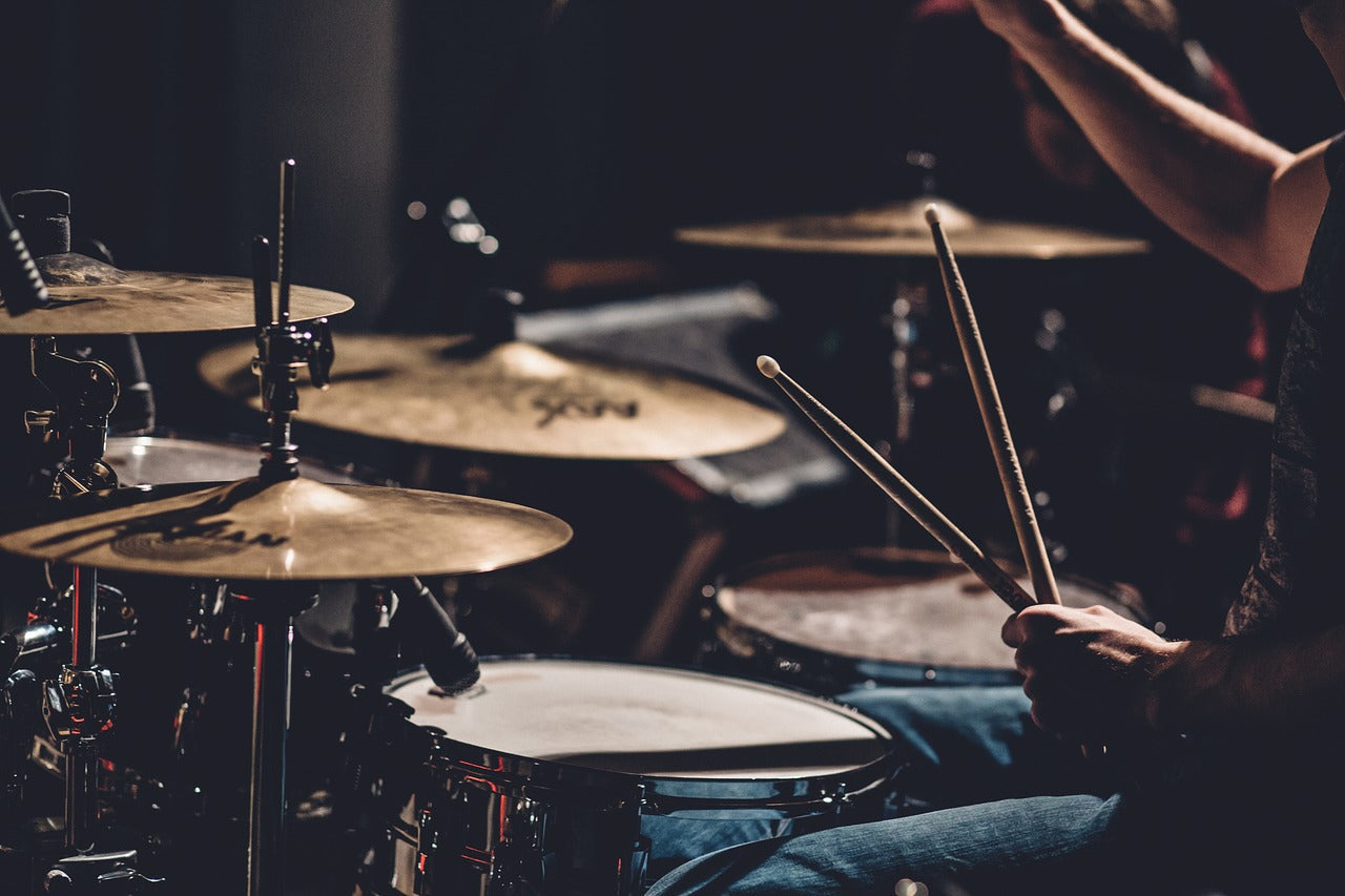 A close-up shot of a drummer's hands holding drumsticks over a snare drum and cymbals
