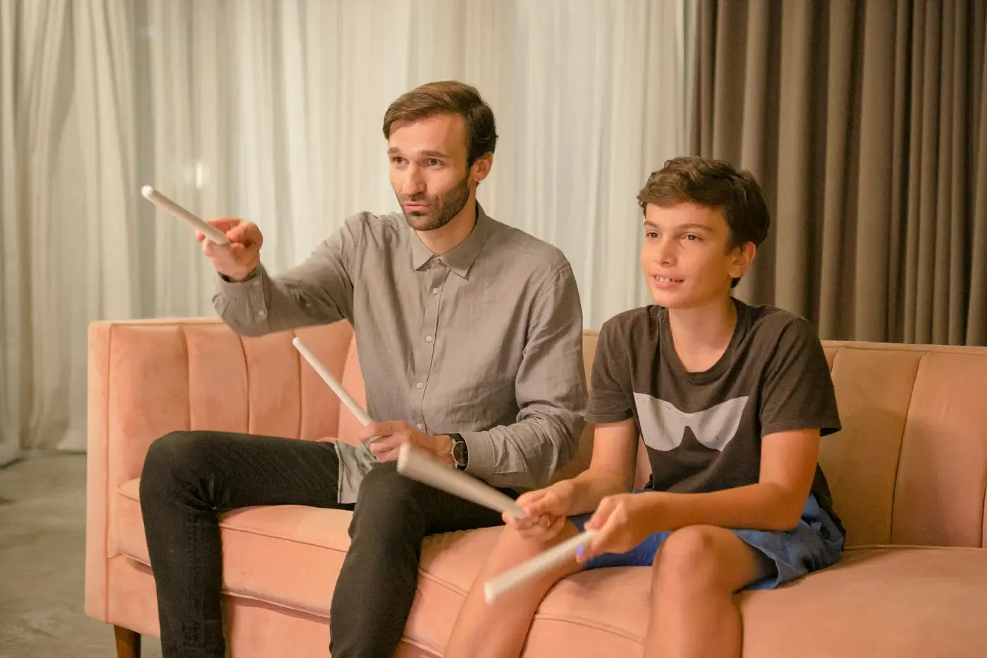 Man and boy playing air drums with PocketDrum 2 Max on a sofa, enjoying a fun rhythm game together at home