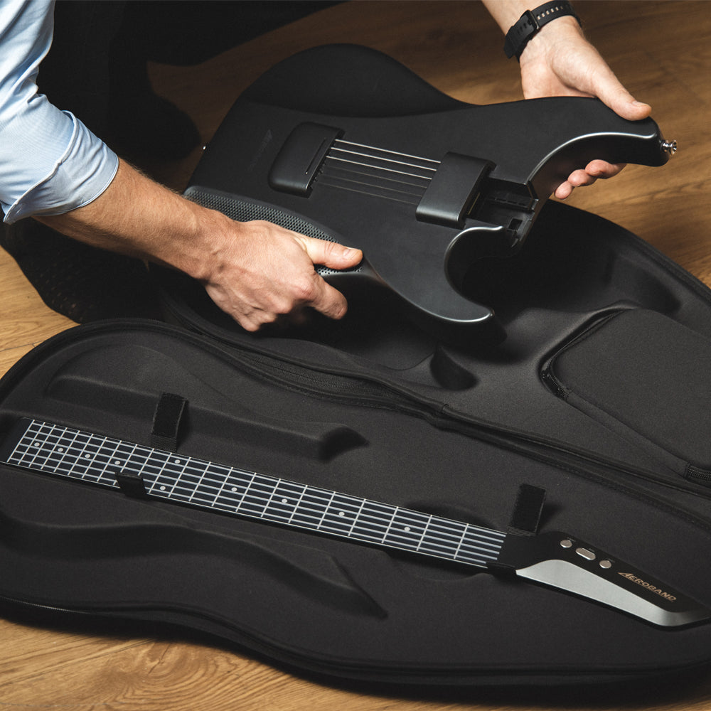 Person places black Aeroband guitar into custom-fit bag, showcasing detachable neck and contoured interior.